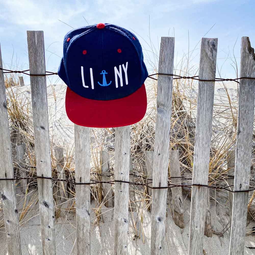 navy red liny long island new york anchor snapback hat outside beach dune fence hanging down shadows close up
